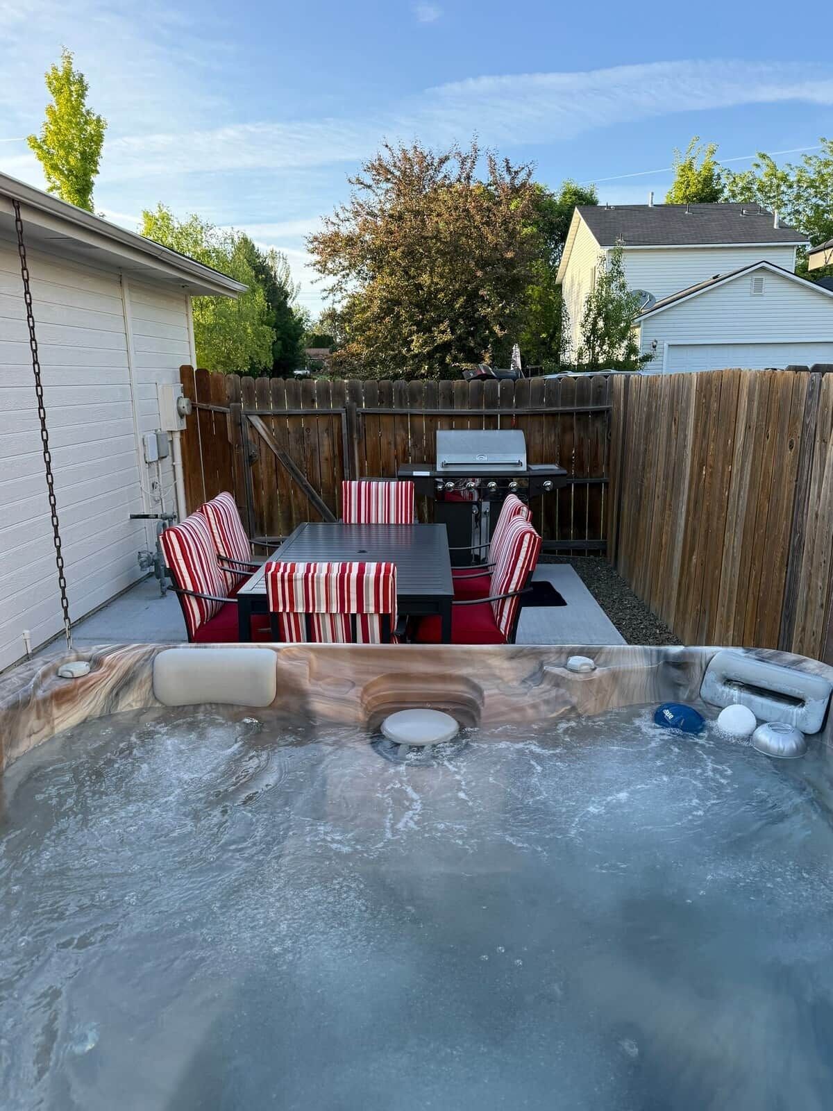 Un jardin avec un jacuzzi, un barbecue et un coin repas agrémenté de coussins à rayures.