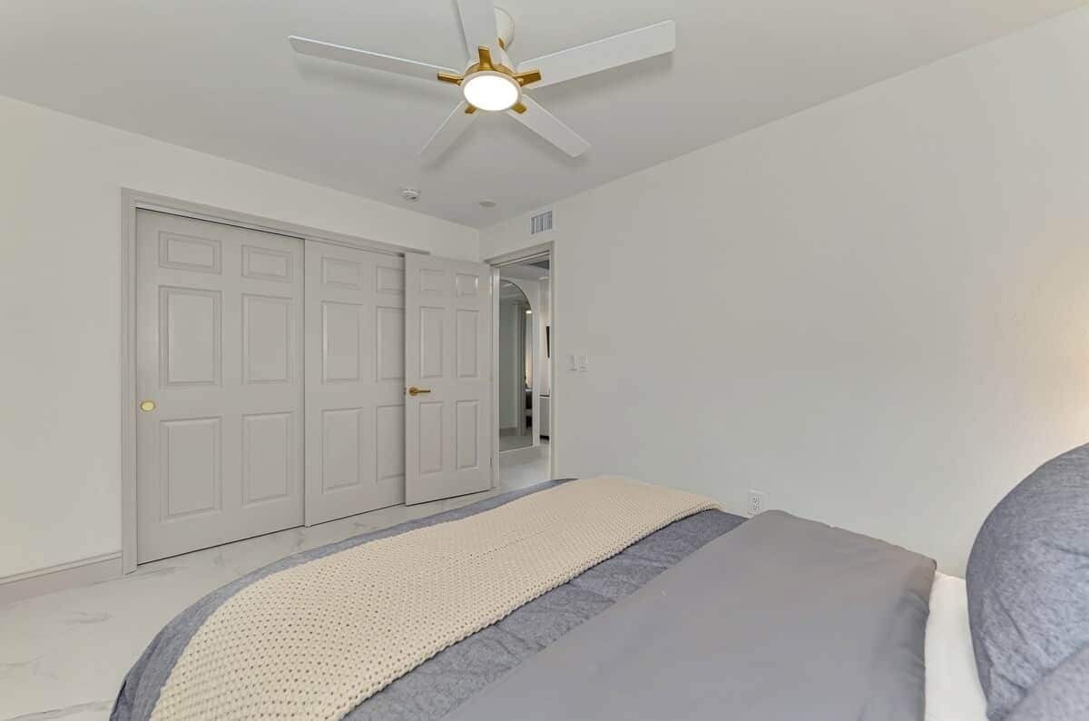 Un dormitorio con cama, ventilador de techo y puerta que da a otra habitación.