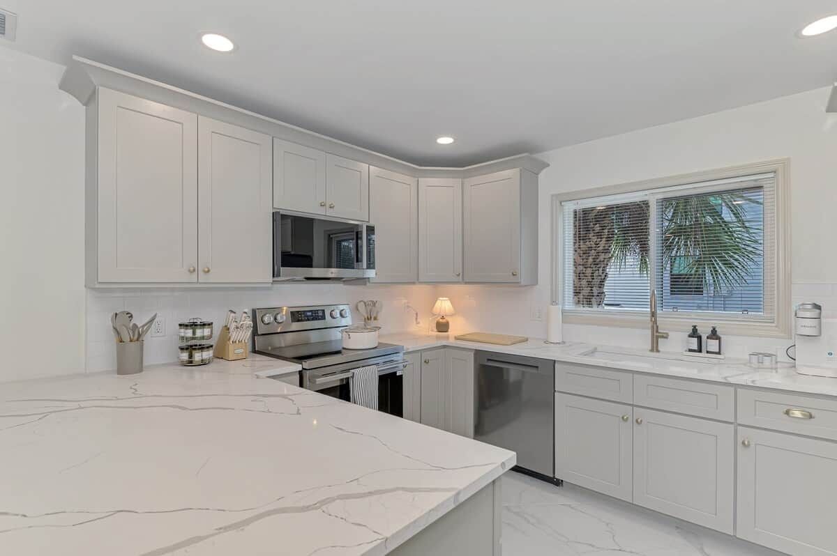 A modern kitchen with white cabinetry, a marble countertop, and a built-in microwave.