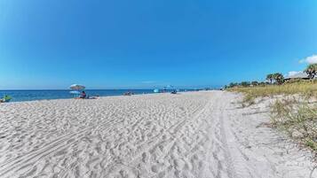 A sandy beach with a clear sky, a few umbrellas, and a few people.