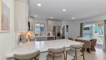 A modern kitchen with a central island, bar stools, and a dining area with a view of a balcony.