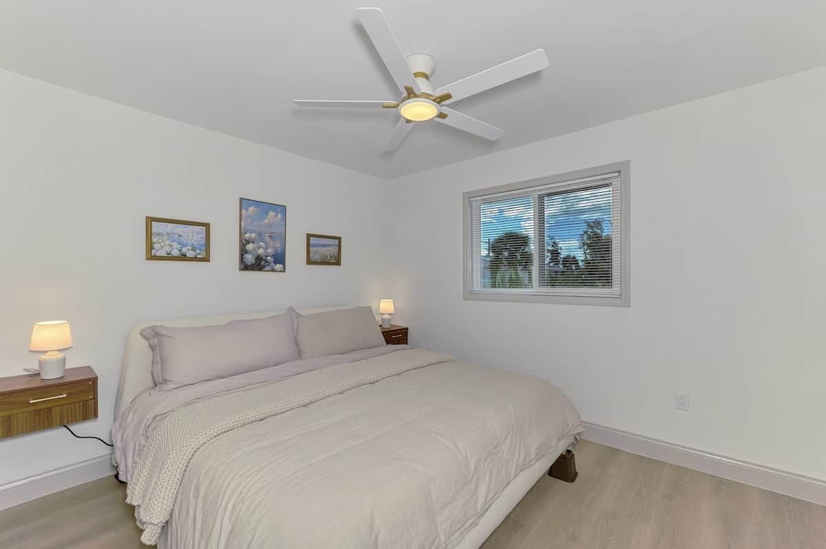 A bedroom with a bed, bedside lamps, a ceiling fan, and a window with blinds.