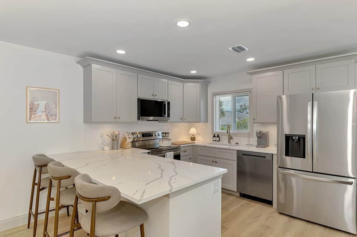 A modern kitchen with white cabinets, a marble island, stainless steel appliances, and bar stools.