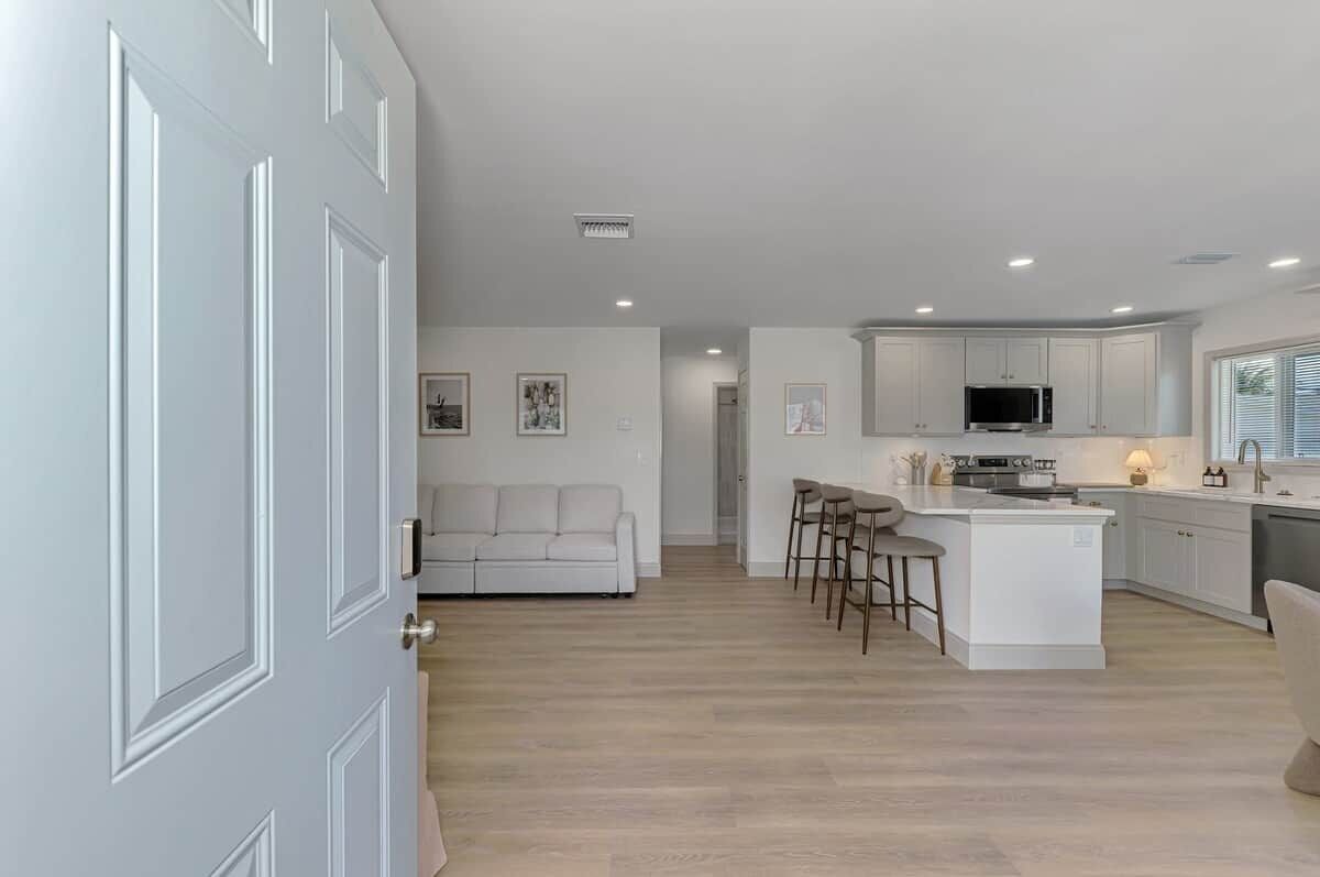 A modern kitchen with white cabinetry, a central island with bar stools, and a dining area with a sofa.