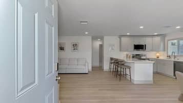 A modern kitchen with white cabinetry, a central island with bar stools, and a dining area with a sofa.