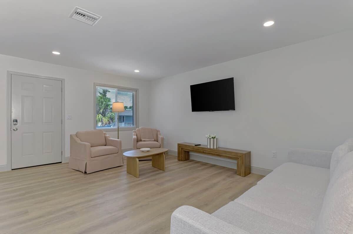 A modern living room with a sofa, two armchairs, a coffee table, and a flat-screen TV mounted on the wall.