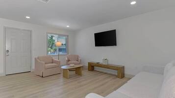 A modern living room with a sofa, two armchairs, a coffee table, and a flat-screen TV mounted on the wall.