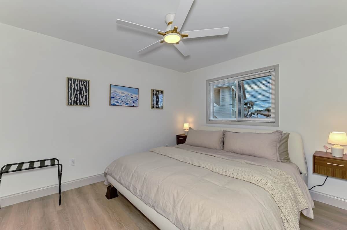 A bedroom with a bed, a ceiling fan, a window with blinds, and wall art.