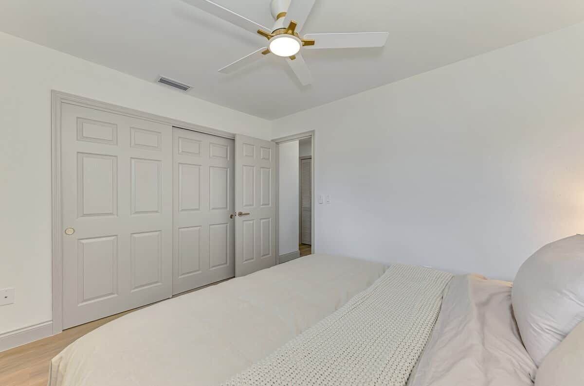 A bedroom with a bed, a ceiling fan, and a door leading to another room.