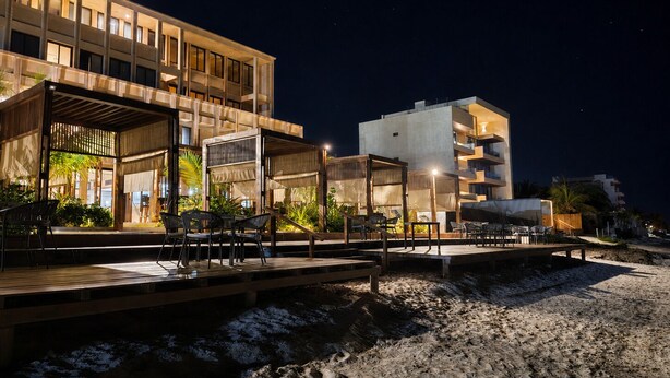 A modern hotel with multiple floors, outdoor seating areas, and a beach view.