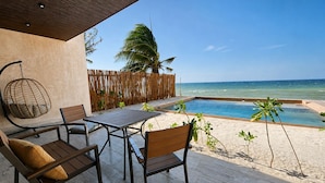An outdoor seating area with a table and chairs, a hanging chair, a wooden fence, and a view of the ocean.