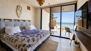 A bedroom with a large bed, a view of the beach, and a sliding glass door leading to an outdoor seating area.