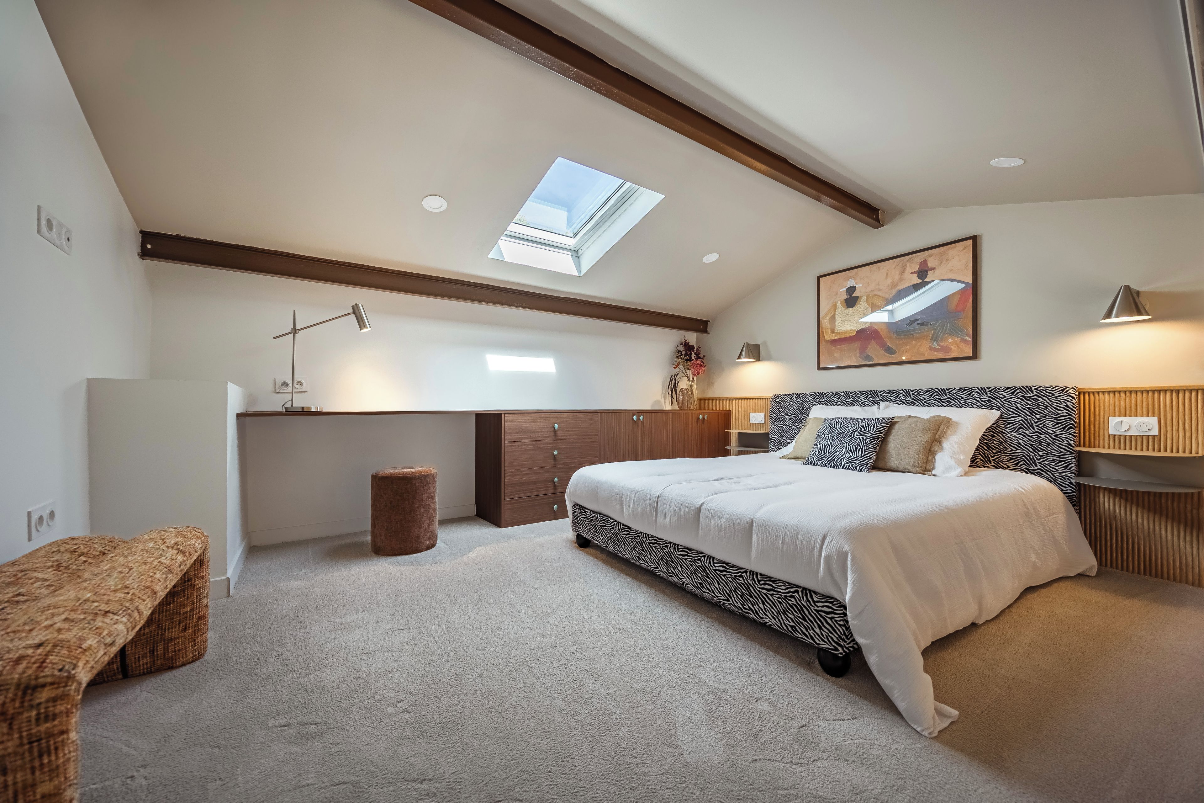 Une chambre avec un puits de lumière, un lit recouvert d’une couvre-lit à motifs zébrés, un bureau et un tableau accroché au mur.