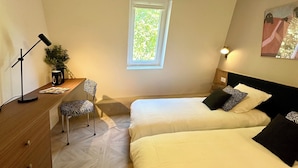 Une chambre avec deux lits, un bureau, une chaise, une fenêtre et un luminaire au plafond.