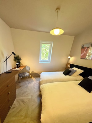 Un dormitorio con dos camas, un escritorio, una silla, una ventana y una lámpara de techo.