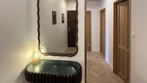 Un couloir avec un grand miroir, une coiffeuse dotée d’un plan de travail en marbre vert et des portes en bois.