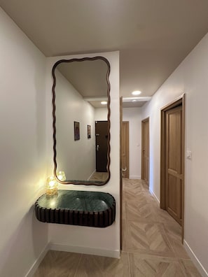 Un pasillo con un espejo grande, un tocador con encimera de mármol verde y puertas de madera.