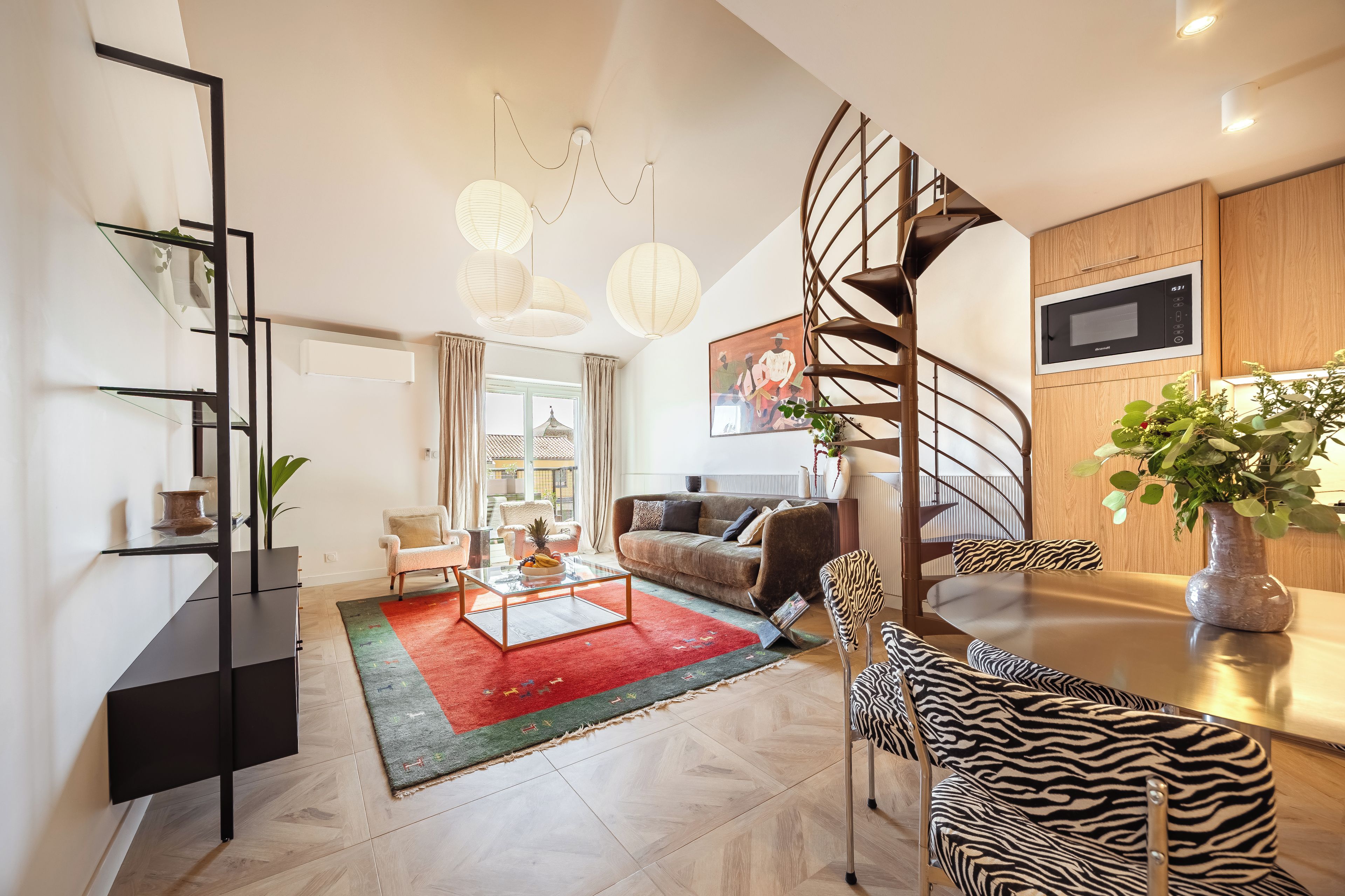 A modern living room with a spiral staircase, a flat-screen TV, and a dining area with zebra-patterned chairs.