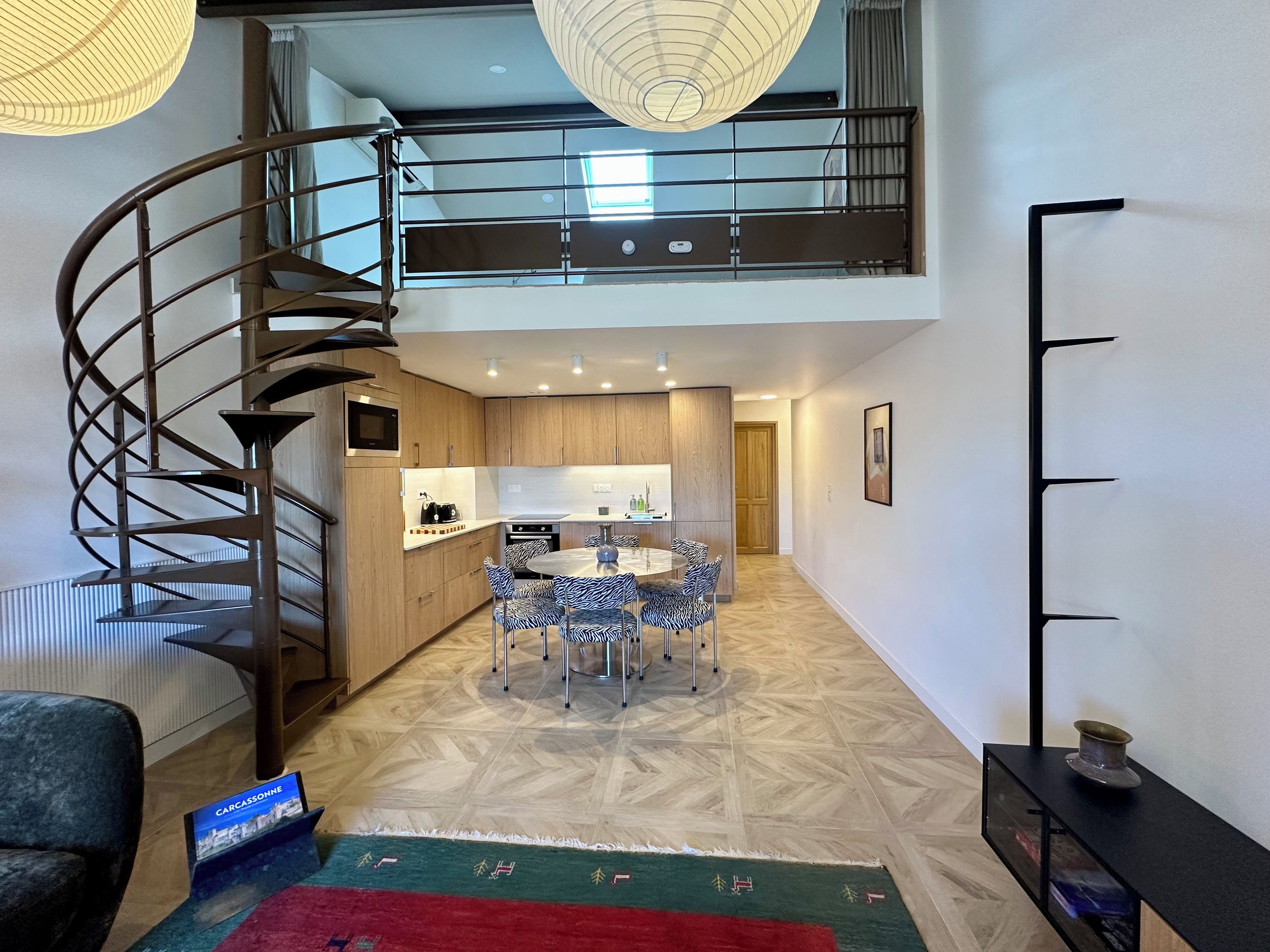 A modern interior with a spiral staircase, a kitchen with a dining area, and a flat-screen TV.