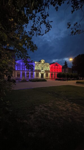A building with classical architecture, illuminated by colored lights, surrounded by a well-maintained lawn and trees. - On the 11th: View of the Medieval City (Carcassonne)