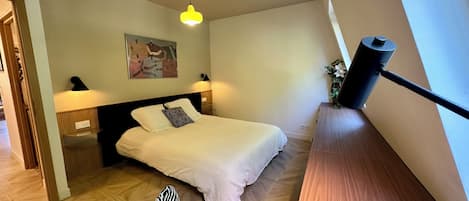 Une chambre à coucher avec un lit, une table de chevet, une lampe, un magazine et un luminaire au plafond.