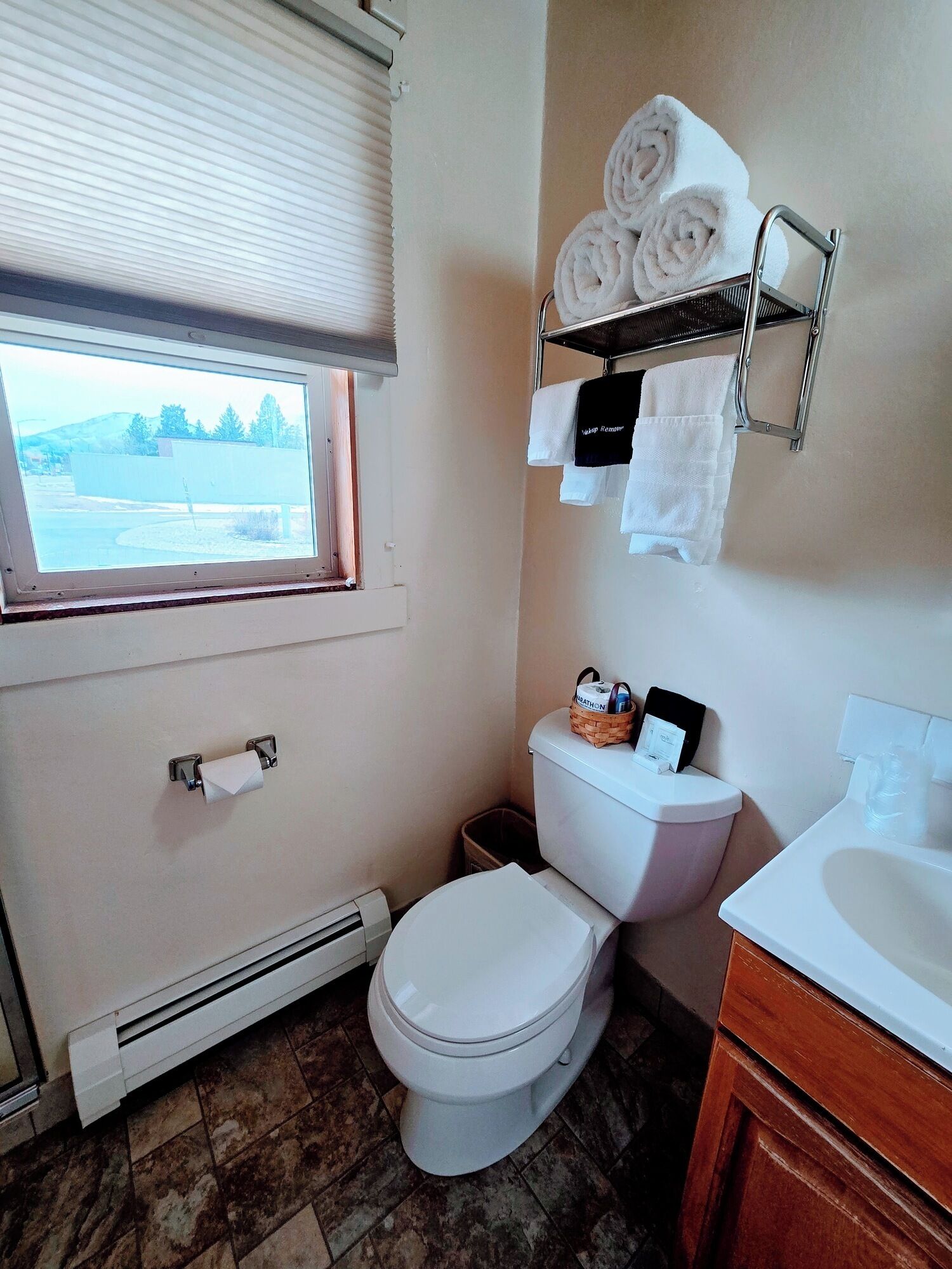 A bathroom with a toilet, a towel rack with towels, a window, and a radiator.