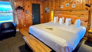 A hotel room with a large bed, a wooden bench, a desk, and a view of the outside.