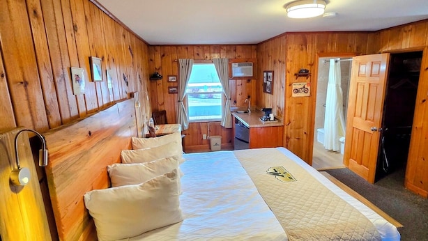 A wooden-paneled room with a bed, a desk, and a bathroom door.