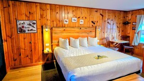 A wooden-paneled room with a large bed, bedside tables, a desk, and a chair.