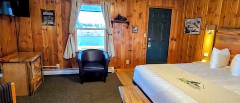 Ett hotellrum med en säng, ett skrivbord, en stol, en bänk, en tv och ett fönster med gardiner.