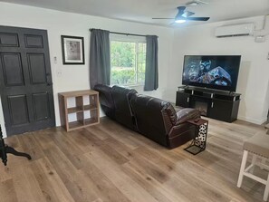 A living room with a leather sofa, a television, and a wooden floor. - Your Own Private Tropical Spring Fed Lake Oasis! (Hudson)