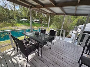 A covered outdoor area with a table and chairs, overlooking a body of water and greenery. - Your Own Private Tropical Spring Fed Lake Oasis! (Hudson)