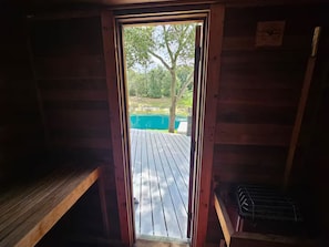 Eine Holzhütte mit einer Bank und einem Metallgestell, eine Tür, die auf eine Terrasse mit Blick auf einen See und Bäume führt.