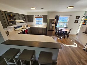 A modern kitchen with a central island, bar stools, a dining area with a table and chairs, and a refrigerator. - Your Own Private Tropical Spring Fed Lake Oasis! (Hudson)