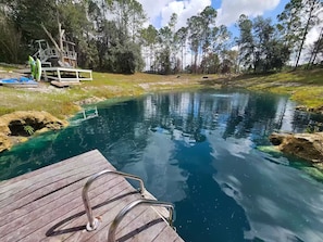 A wooden dock leading into a clear blue pond surrounded by trees. - Your Own Private Tropical Spring Fed Lake Oasis! (Hudson)