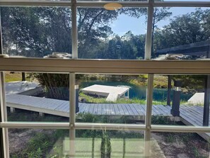 Blick durch ein Fenster auf einen Deckbereich mit Holzterrasse und Teich.