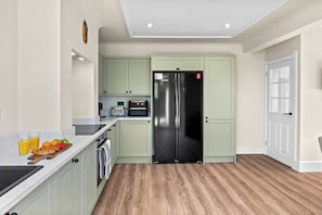 A modern kitchen with light green cabinets, a stainless steel refrigerator, and a wooden countertop with fruits and a toaster. - Comfortable Coastal Home near Meols Beach, perfect base with parking (Meols)