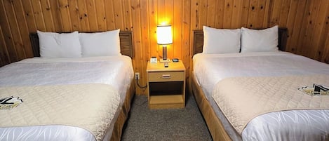 Ett rum med två sängar, en väggpanel av trä, ett nattduksbord med en lampa och en väggklocka.