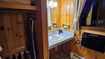 A wooden cabin bathroom with a sink, mirror, and heater.