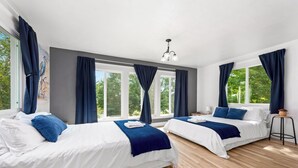 Camera d'albergo con due letti, ampie finestre, una lampada a soffitto e un tavolino.