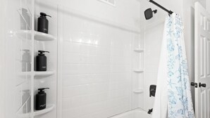 Un bagno con pareti piastrellate di bianco, una vasca e una doccia con tenda a tema marino.
