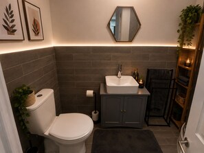 Et badeværelse med toilet, vask og skab, med mørke fliser og et spejl.