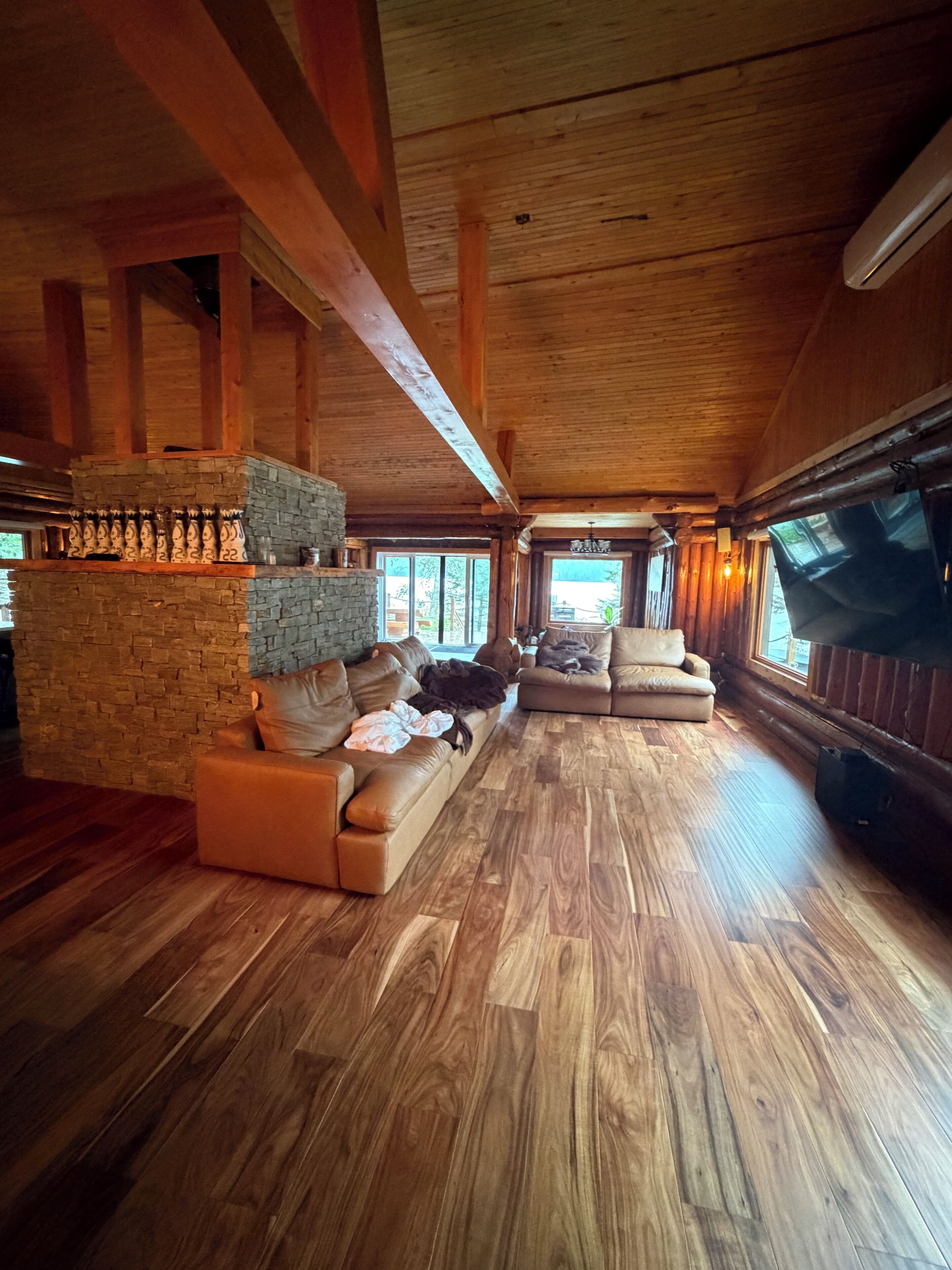A spacious living room with wooden floors and a stone fireplace. There are two sofas and a television.