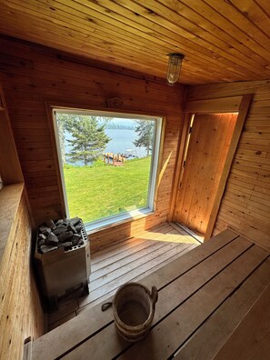 A wooden cabin with a large window overlooking a grassy area and a body of water. - Lakefront Paradise on 31 Mile Lake With Hot Tub, Sauna & More! (Ste Thérèse de la gatineau)