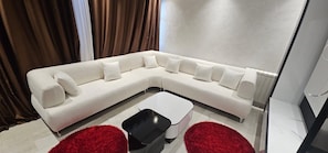 A modern living room with a white sectional sofa, a black coffee table, and red accent pillows.