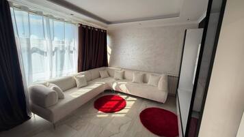 A modern living room with a sectional sofa, a red rug, and a large window with curtains.