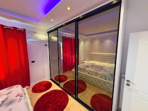A bedroom with a sliding glass door, a bed with a floral bedspread, and red circular rugs on the floor.