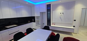 A modern kitchen with white cabinetry, a black countertop, and a dining area with a white table and black chairs. - Elegant Modern Retreat with Stylish Comfort (Shkodër)
