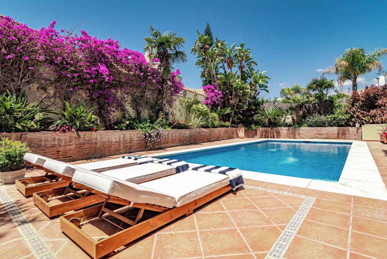 Une piscine entourée de chaises longues et bordée d’un mur de briques recouvert de plantes à fleurs.