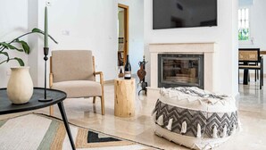 Een woonkamer met een bank, een salontafel, een open haard en een aan de muur bevestigde televisie.